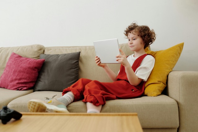 A child sitting on the couch on their device.
