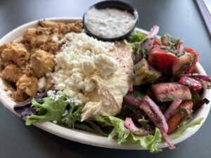 Bowl with proteins, greens, toppings and sauce.