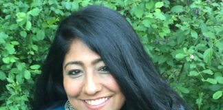 Headshot of woman in blue shirt against green foliage background