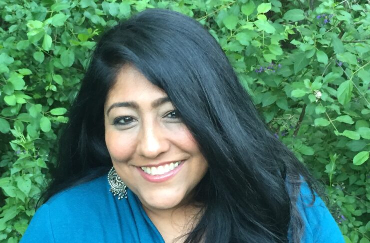 Headshot of woman in blue shirt against green foliage background