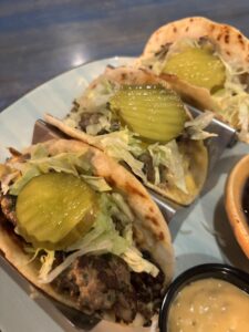 Smash burger tacos, topped with cheese, lettuce and pickles.